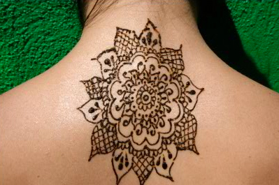 A close-up of a detailed henna design on the back of a person's neck against a green background.