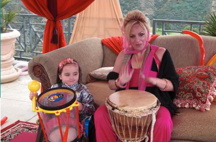 A woman and a young girl playing drums on a terrace with lush greenery in the background.