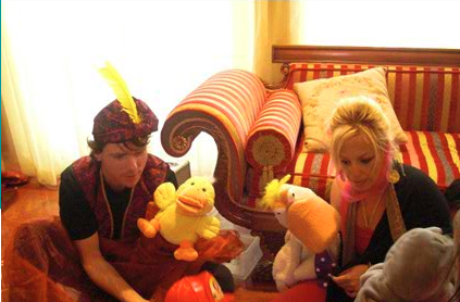 Two people in colorful costumes sitting on the floor with plush toys, engaging playfully in a brightly lit room.