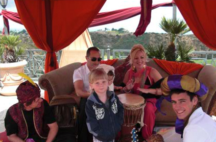 A family with three adults and two children enjoying time together under a red canopy, one child in the center looks at the camera while others engage with musical instruments.