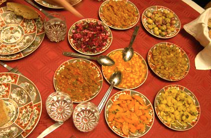 A variety of indian dishes served in ornate bowls on a red tablecloth, including curries, rice, and salad.