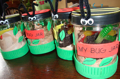 Four homemade "bug jars" decorated with green tape and googly eyes, containing sand and artificial bugs, with labels such as "my bug jar.