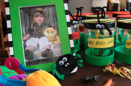 A table with items including a child's photo in a green frame, bug-themed jars labeled "my bug jar," and colorful craft projects.