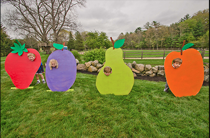 Children peeking through colorful fruit-shaped cutouts at a park.