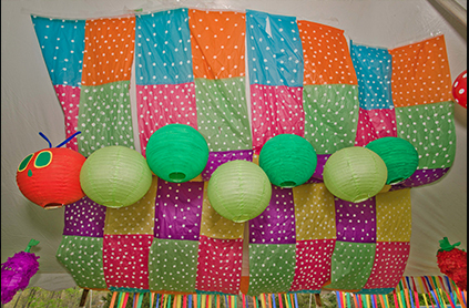 Colorful quilted backdrop with polka dots and several hanging green paper lanterns at a festive event.