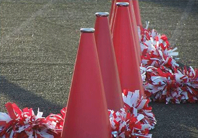 Four red traffic cones lined up on asphalt, surrounded by red and white pom-poms.