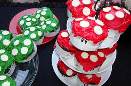 Cupcakes decorated to resemble mushrooms from the super mario series, with red and green icing and white spots, displayed on tiered stands.