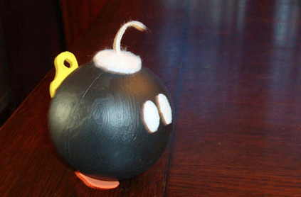 A small, black, cartoon-style bomb with a lit fuse, white spark eyes, and an orange nose, placed on a wooden table.