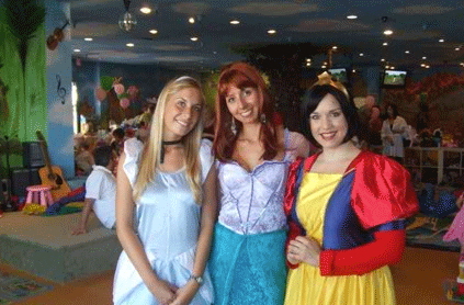 Three women posing at a children's party, one in casual clothing and two dressed as princesses, with a colorful, balloon-filled background.