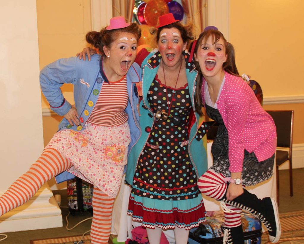 Three clowns in colorful, mismatched costumes striking playful poses at an indoor event.